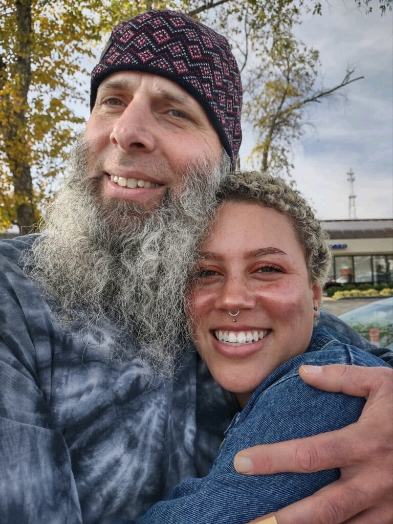 A middle aged man with a white beard hugging a middle aged woman with a nose ring and short curly hair