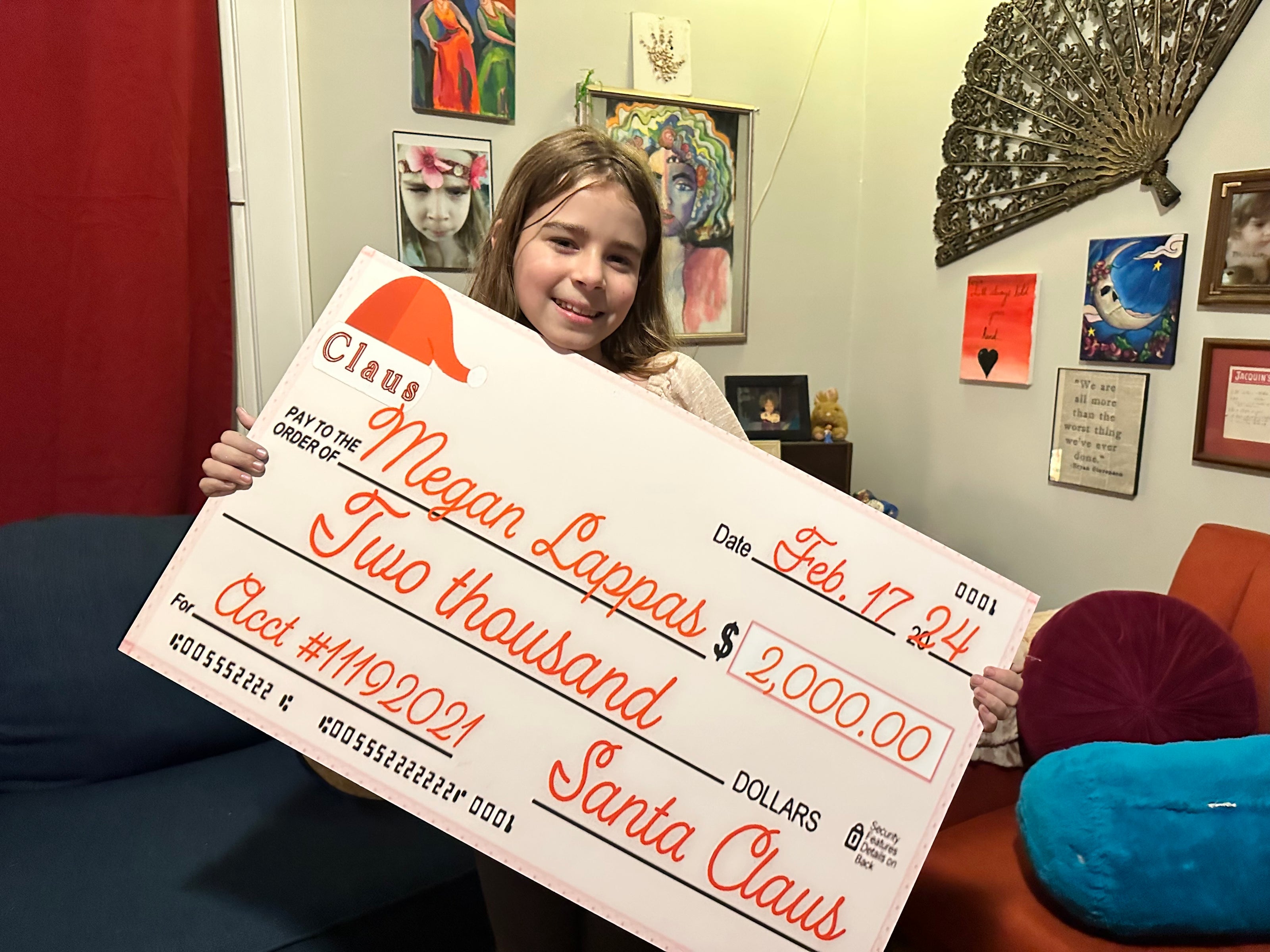 a young girl holding a large check for 2000 dollars in front of a wall with many decorations 