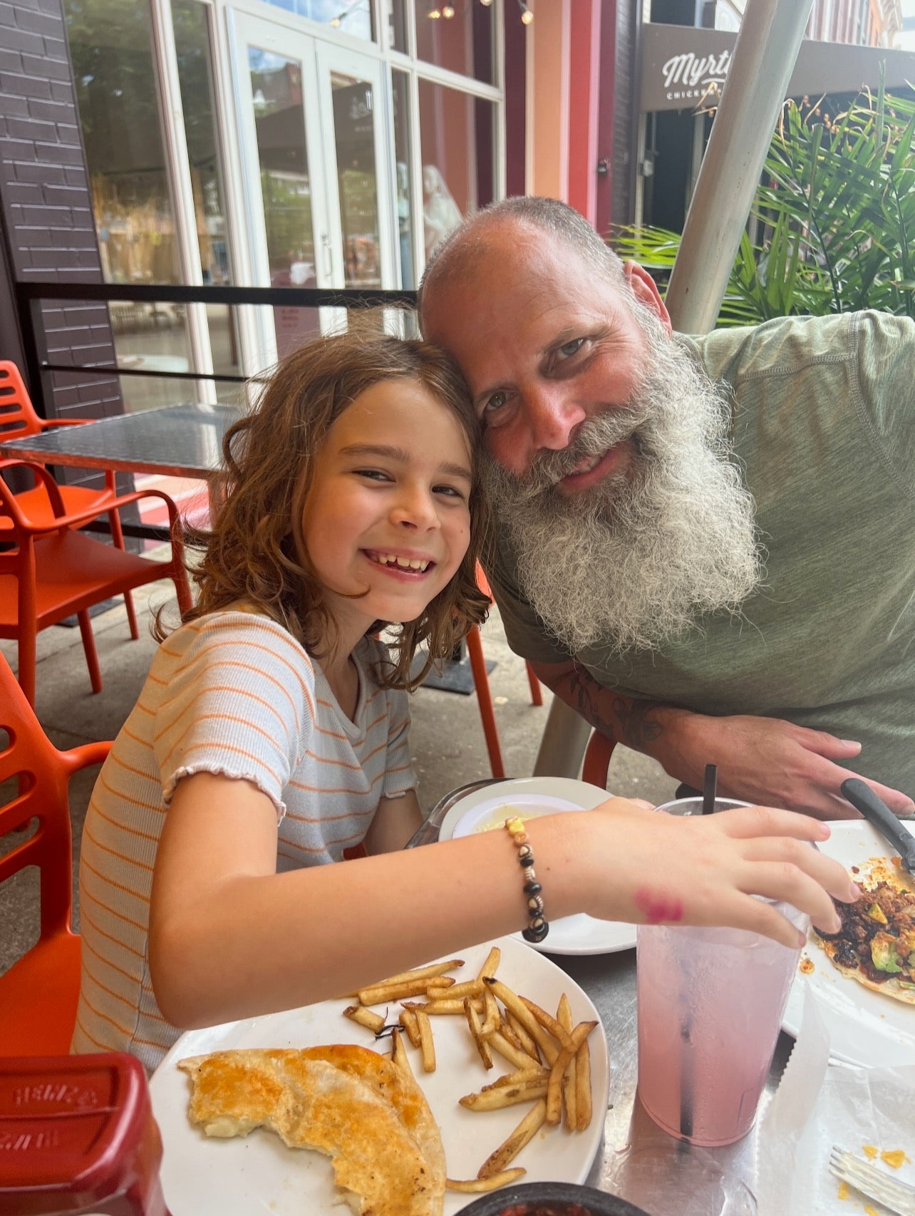 A middle aged man with a big fully white beard leaning in next to a young girl at a dinner table at a restaraunt