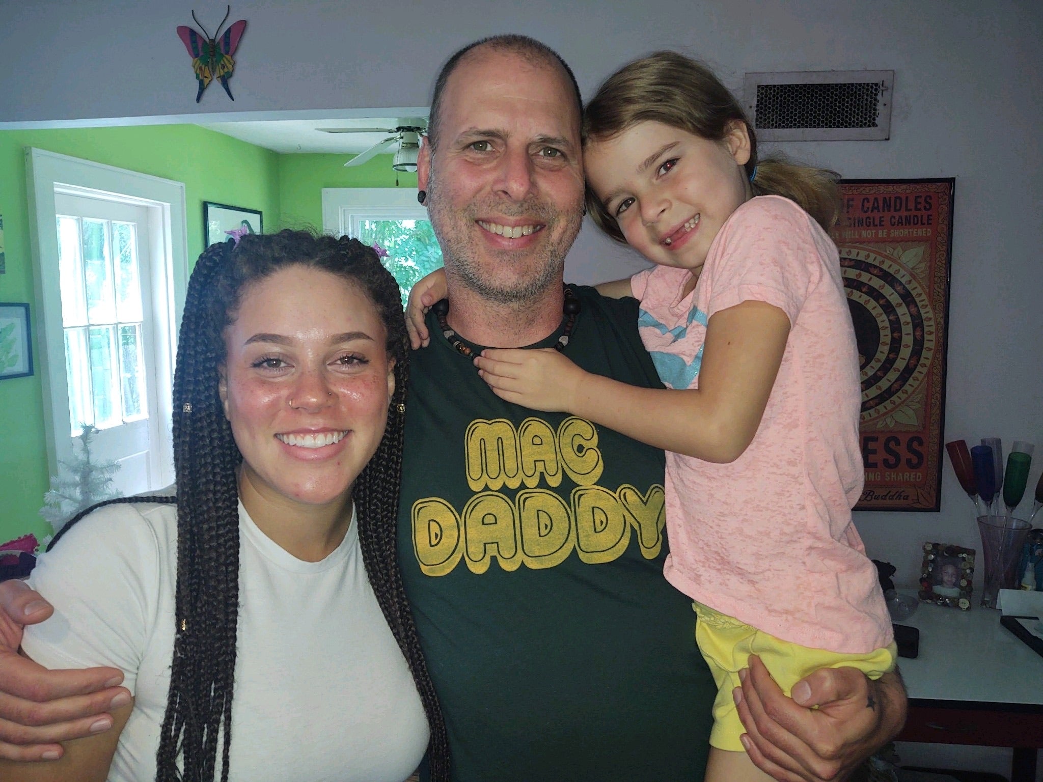 a bald middle aged man with earrings, a middle aged woman with braided hair, and a very young girl being held by the man.