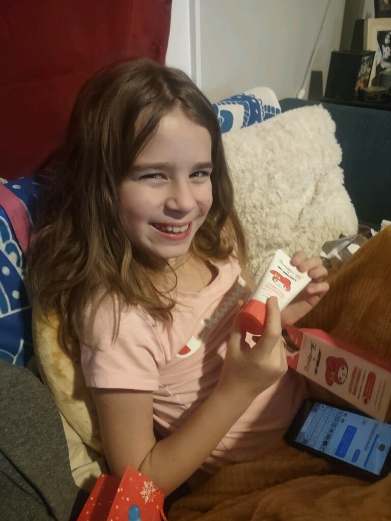 A young girl smiling and sitting on a couch holding a tube of a product