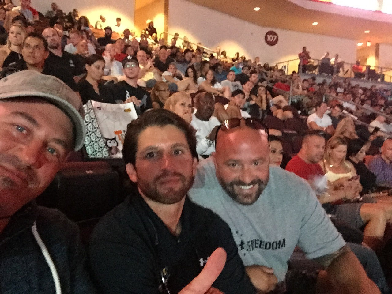 3 men sitting in a crowd smiling. two of them have beards, one has sun glasses on, and another has a hat on. the man with a hat is wearing a gray hoodie. the. man first man with a beard is wearing ia black quarter zip, and the last man with sunglasses is wearing a gray shirt with the text "freedom" on it.